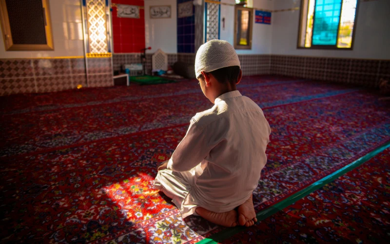 Young boy in traditional attire praying in mosque