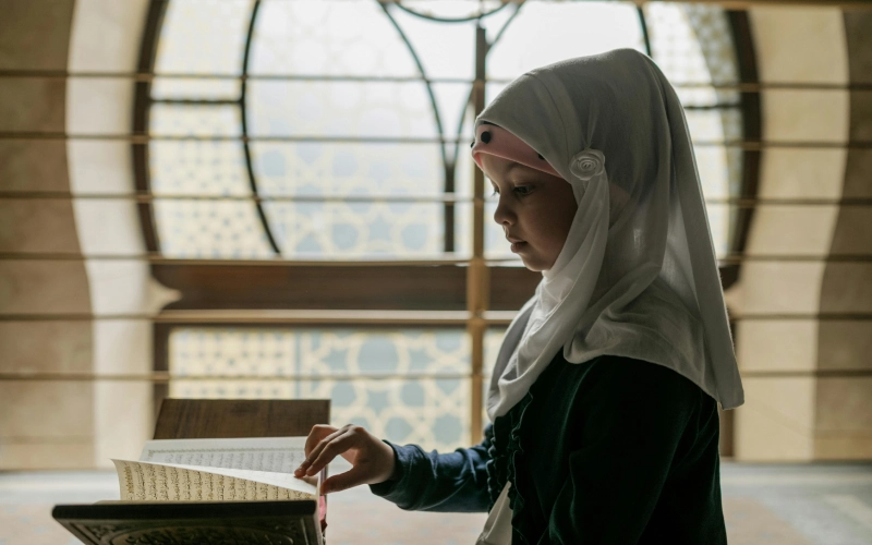 Young girl in hijab reading Quran in mosque