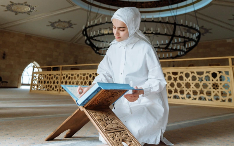 Woman in modest white dress reading book in mosque