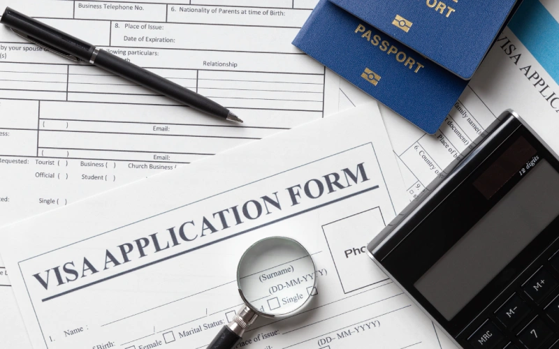 Visa application form, magnifying glass, passports, pen, calculator